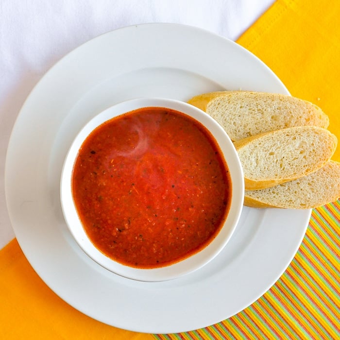 Roasted Tomato Fennel Soup wide shot of a serving in white bowl with baguette on the side