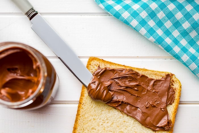 Photo of nutella being spread on white bread.