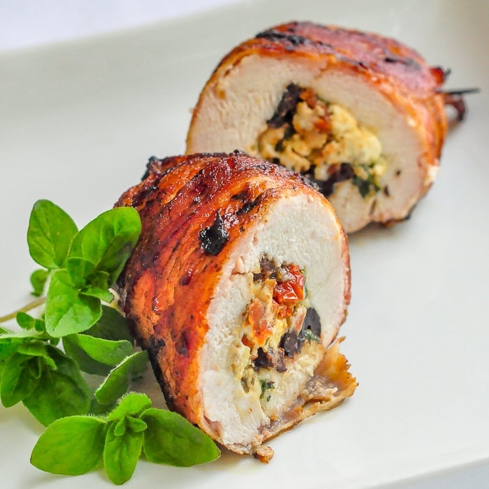 Bacon Wrapped Mediterranean Stuffed Grilled Chicken on a white plate with fresh oregano garnish