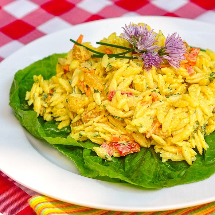 Creamy Curry Orzo Salad on a bed of lettuce on a white plate