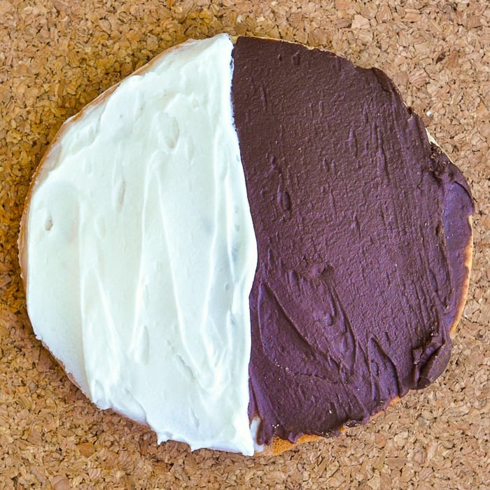 The Best Black and White Cookies close up overhead shot of a single cookie on a cork background