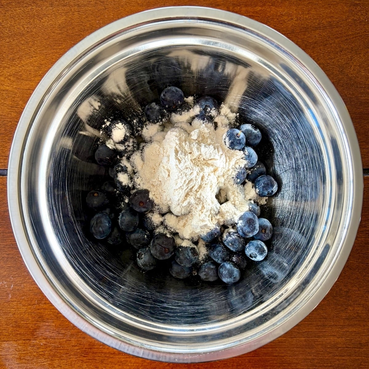 Photo of blueberries in a stainless steel bowl with two tablespoons of flour on top