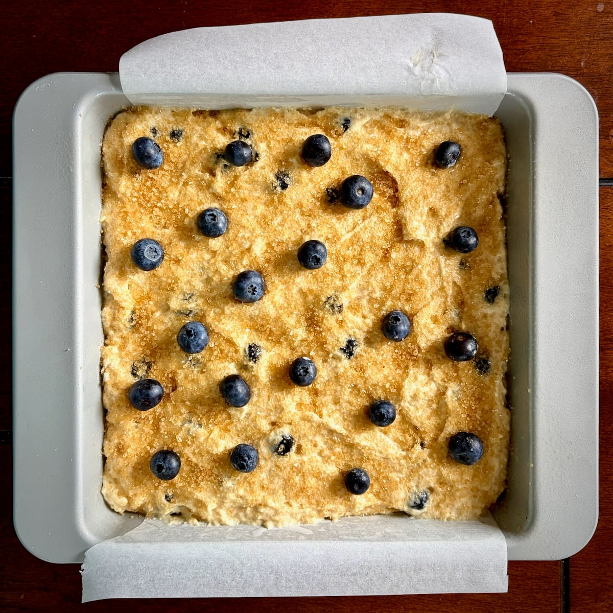 Overhead photo of sugar and blueberries on top of the batter in a square pan ready for the oven