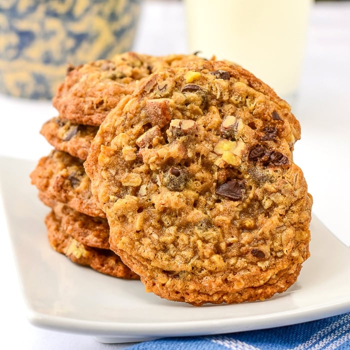 Chocolate Pecan Crunch Cookies stacked on a white plate with a glass of milk in the background