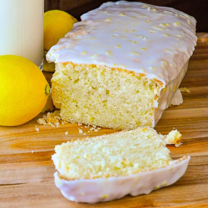 Glazed Lemon Pound Cake on a wooden cutting boards with lemons and a glass of milk on the side