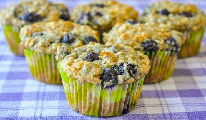 Blueberry Oatmeal Lemon Cheesecake Muffins wide shot of 6 muffins on a blue checkered table cloth