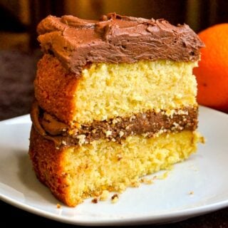 Photo of one slice of Orange Velvet Cake on a white plate with oranges in background