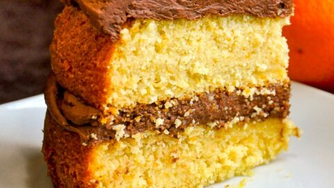 Photo of one slice of Orange Velvet Cake on a white plate with oranges in background