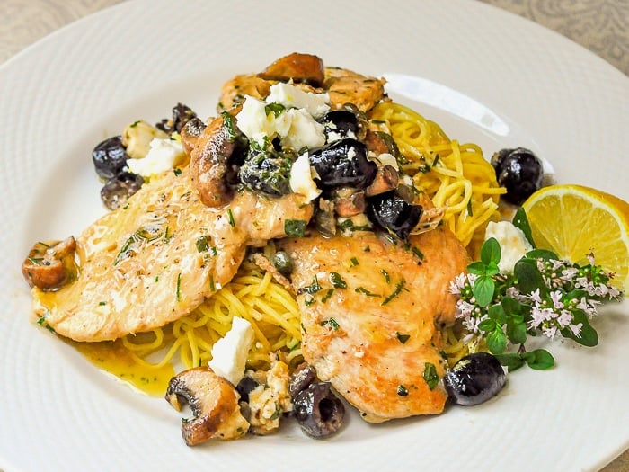 Mediterranean Lemon Butter Chicken pictured with oregano flowers and lemon wedge on a white plate