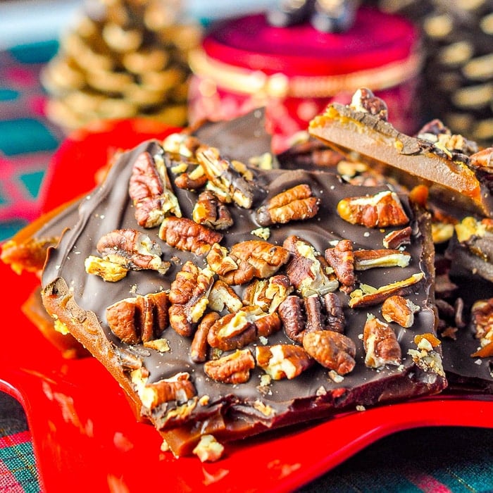 Chocolate Toffee Pecan Brittle pictured on a red plate with Christmas decorations in the background.
