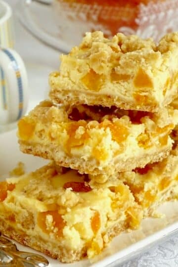 Apricot Amaretto Cheesecake Bars stacked on a white and silver plate.