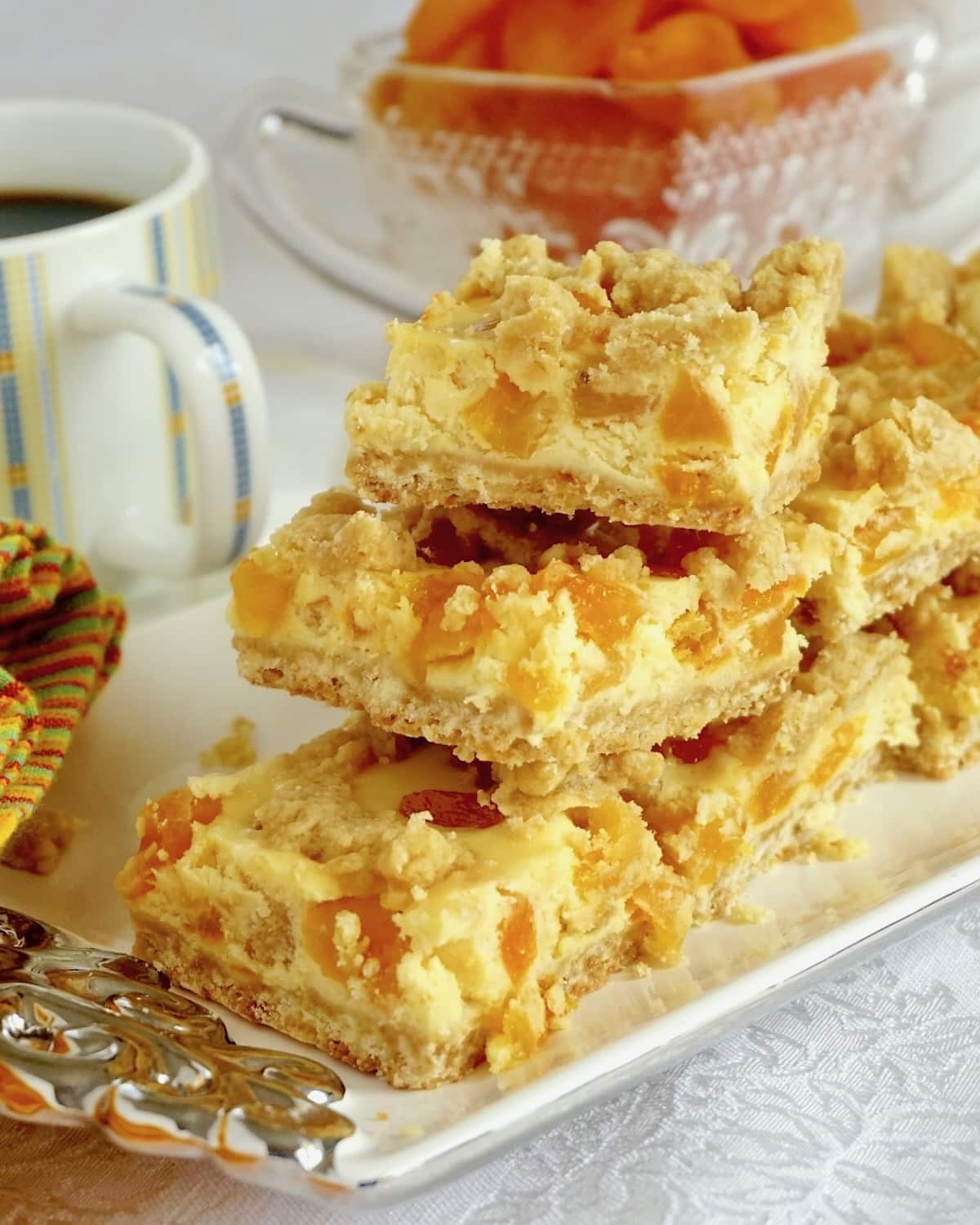 Apricot Amaretto Cheesecake Bars stacked on a plate with coffee service in the background.