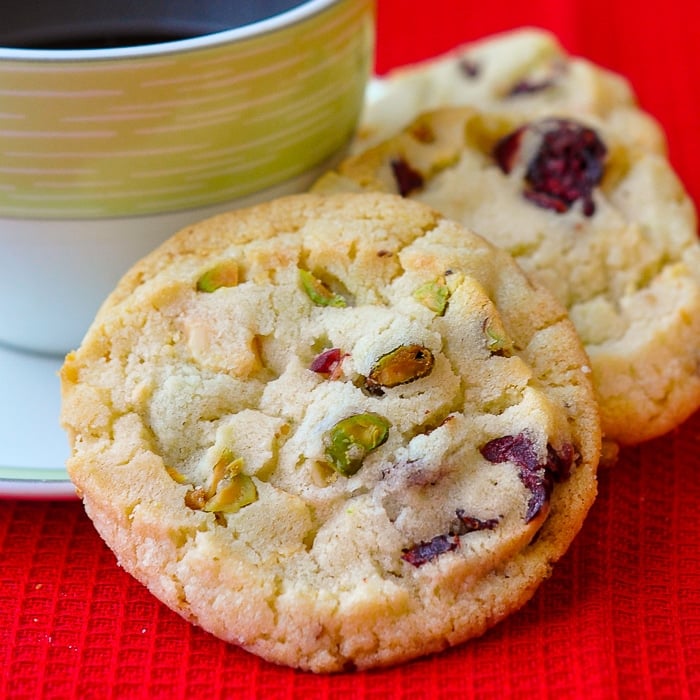 Pistachio White Chocolate Cranberry Cookies close up photograph of cookies with a cup of coffee on red background