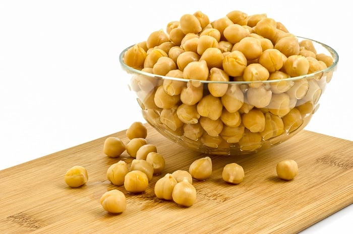 Washed and drained canned chick peas in glass dish on bamboo board isolated on white background. Stock Photo