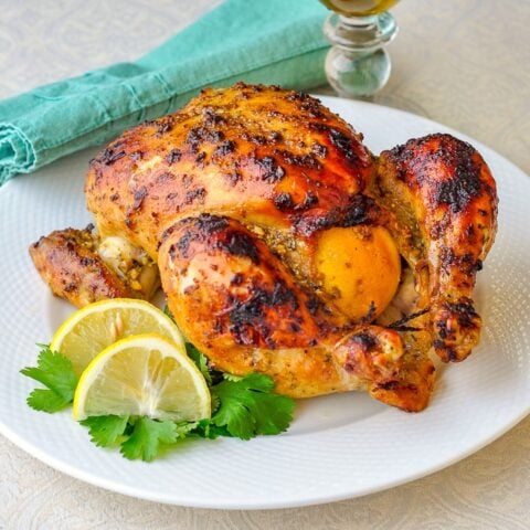 Dijon Roasted Lemon Chicken photo of whole roasted chicken on a white plate with lemon and parsley garnish