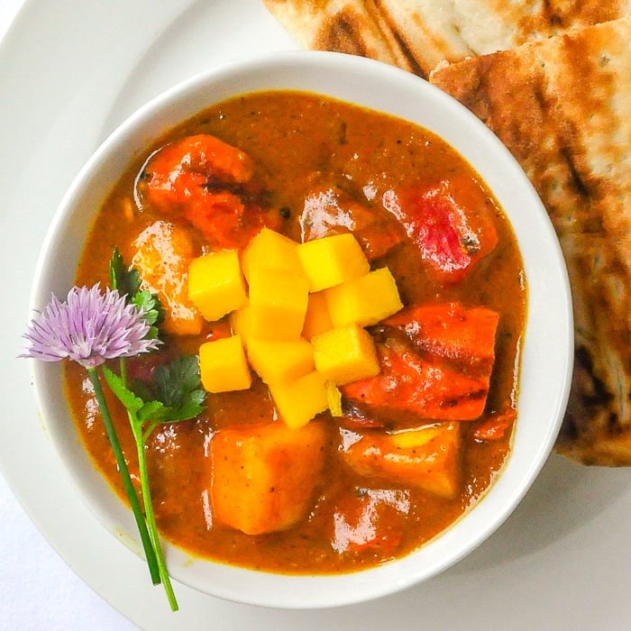 Easy Mango Chicken Curry close up photo of single serving in white bowl with Naan on the side