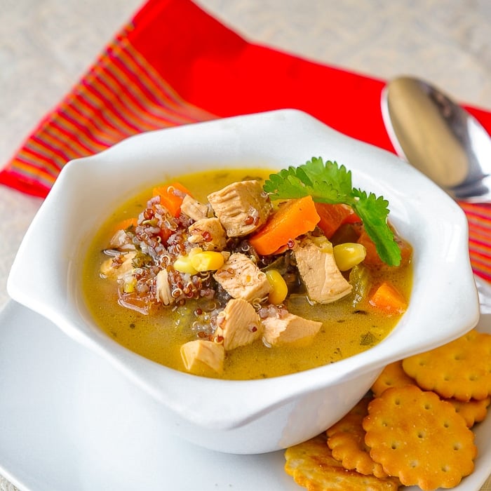 Lemon Chicken Soup with red quinoa and thyme shoyn in a white bowl with crackers on the side.