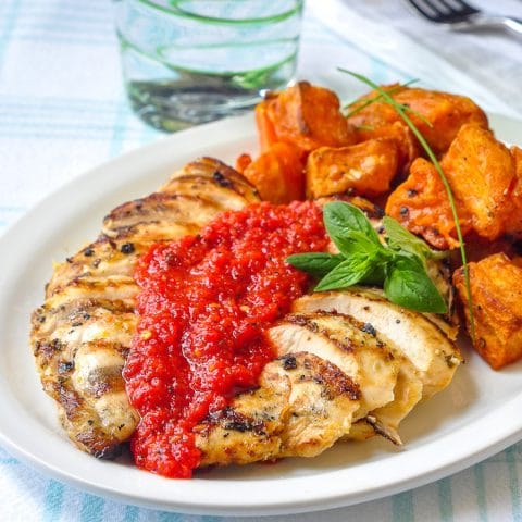 Lemon Herb Grilled Chicken with Spicy Roasted Red Pepper Sauce shown with roasted sweet potatoes on a white plate.