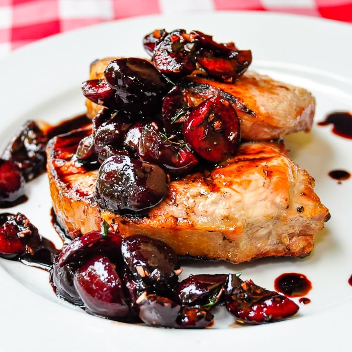 Two Grilled Pork Chops with Balsamic Thyme Cherries on a white plate