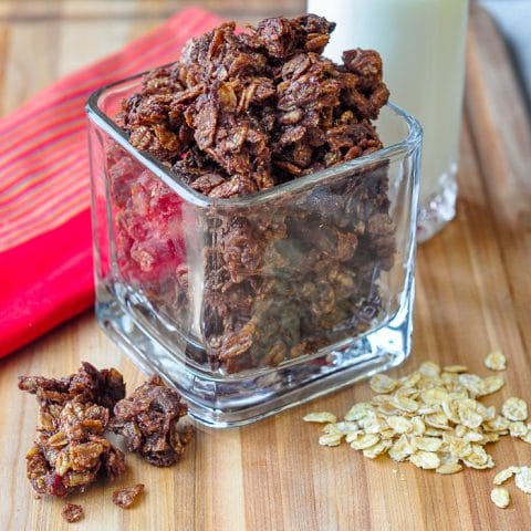 Chocolate Kamut Granola in a clear glass container on a wooden cutting board