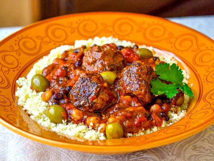 photo of Moroccan Meatball Stew in an orange patterned bowl with couscous