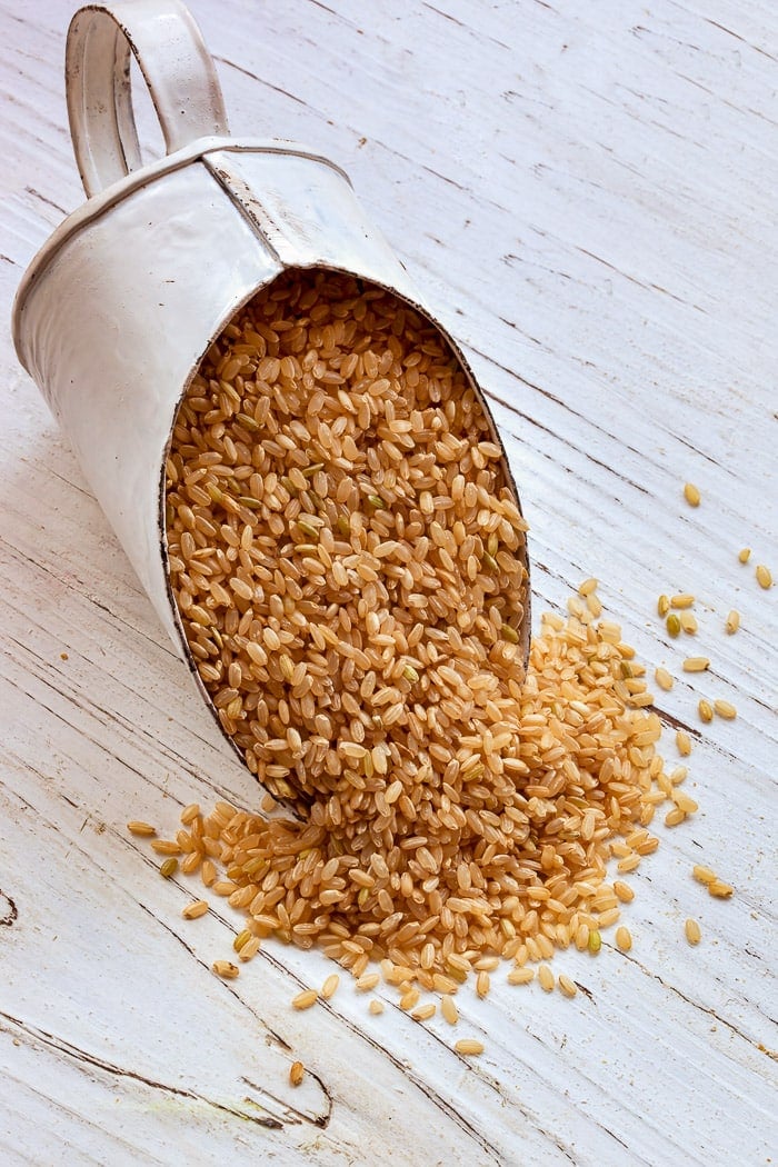 Scoop of brown rice over rustic timber background.