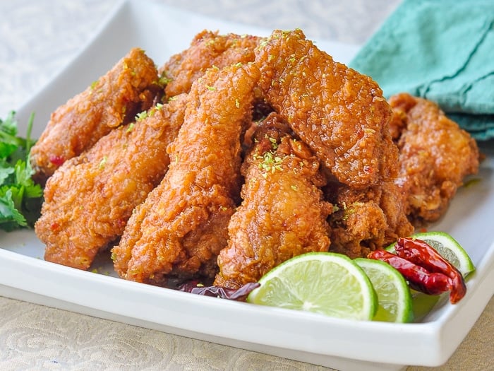 Chili Lime Sticky Crispy Chicken Wings on a white serving platter with chili and lime garnishes