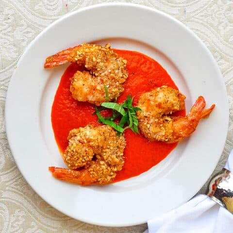 Almond Crusted Shrimp with Roasted Red Pepper Sauce pictured on a white plate with chopped basil garnish