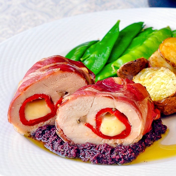 Prosciutto Wrapped Chicken Breasts on a white plate with green beans, tapinade and potatoes