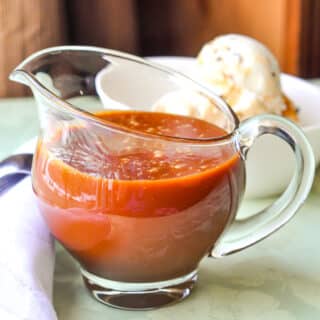 Homemade Caramel Sauce pictured in a glass jug with ice cream in the background