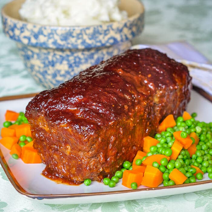 Old Fashioned Meatloaf with sweet onion glaze shown on seving platter with peas and carrots.