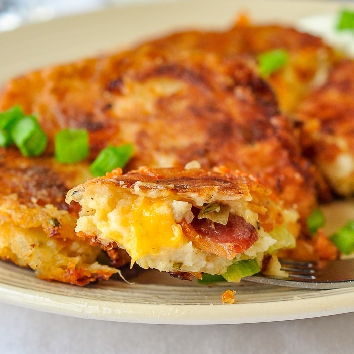 Onion Cheddar and Bacon Potato Cakes photo of single bite on a fork showing bacon and melted cheese on the interior of the finished potato cake