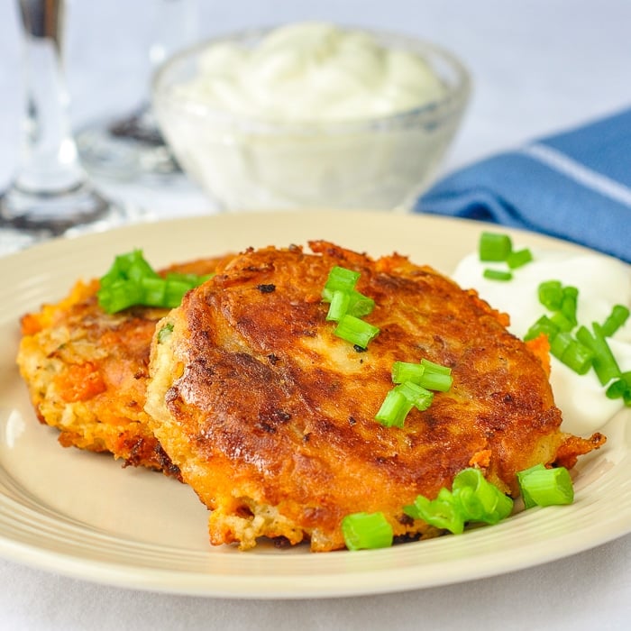 Onion Cheddar and Bacon Potato Cakes photo of two potato cakes on a beighe plate with sour cream in the background