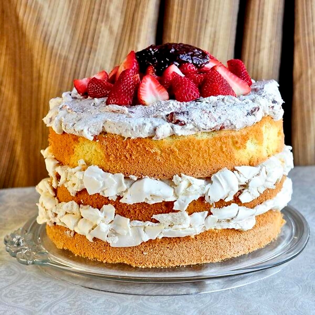 Strawberry Fool Pavlova Cake photo of full uncut cake on a clear glass serving plate.