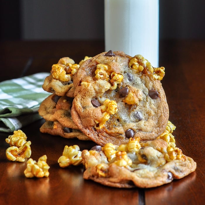 Caramel Corn Chocolate Chip Cookies on a wooden table with a glass of milk and napkin