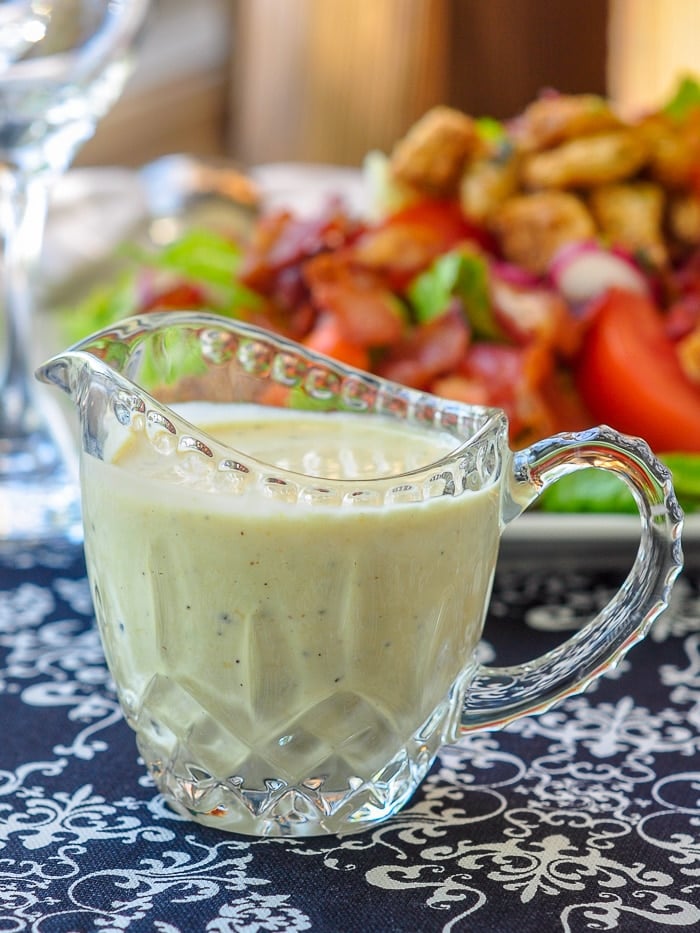 Creamy Dijon Dressing in a small glass jug with BLT salad in the background.