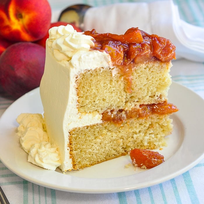 Roasted Peaches and Cream Cake photo of a singe slice on a white plate with fresh peaches in the background