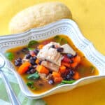 Barbecue Chicken Soup with black beans in a square bowl with roll on the side