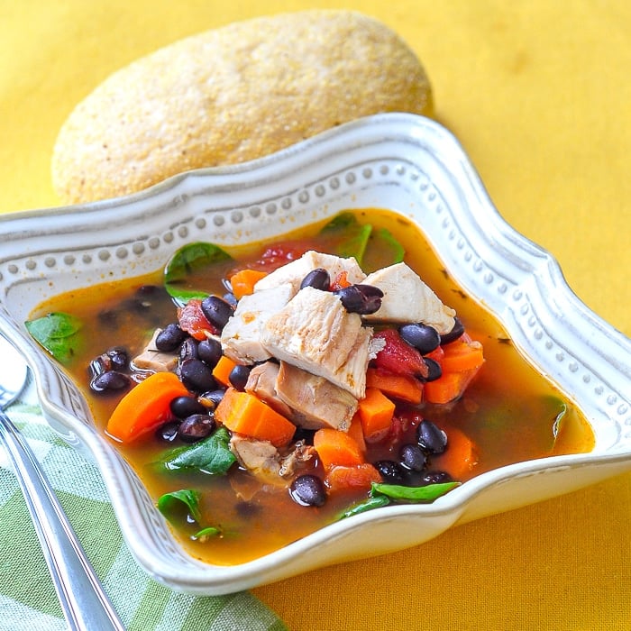 Barbecue Chicken Soup with black beans in a square bowl with roll on the side