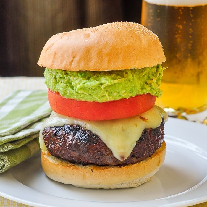 Chorizo Pepper Jack Cheeseburgers with Guacamole photo of a single completed burger with a glass of beer in the background