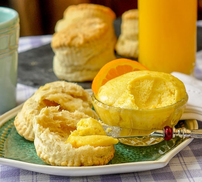 Maple Orange Butter being spread on a biscuit with coffee, biscuits and OJ on the side