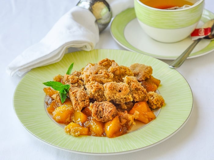 Mango Peach Coconut Crumble on a green plate with a cup of tea in the background