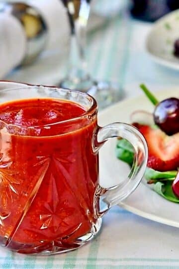 Roasted Red Pepper Salad Dressing. Photo of dressing in a clear glass jug with mixed salad on a plate beside.