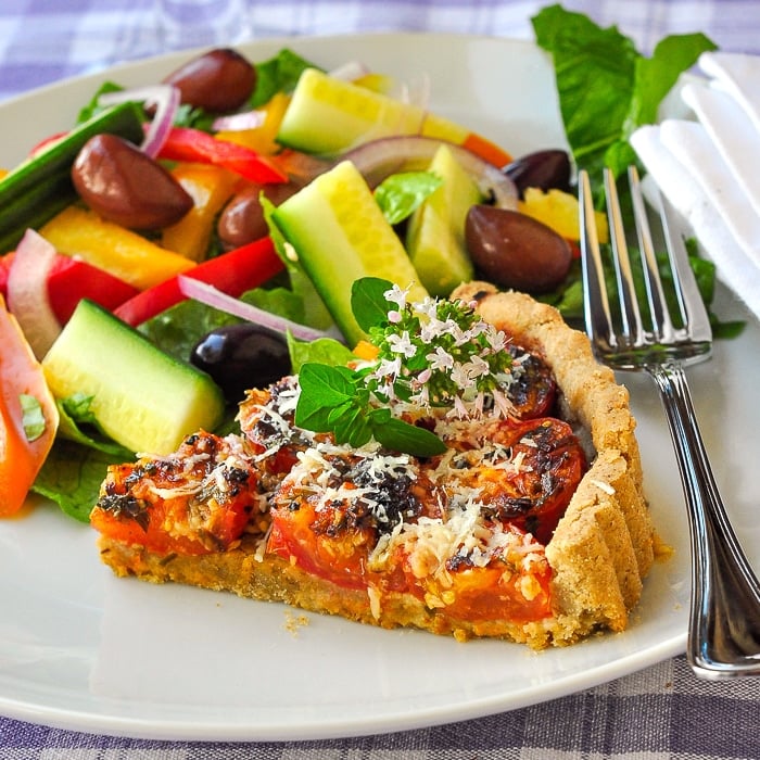 Photo of one slice of tomato parmesan tart with side salad on a white plate