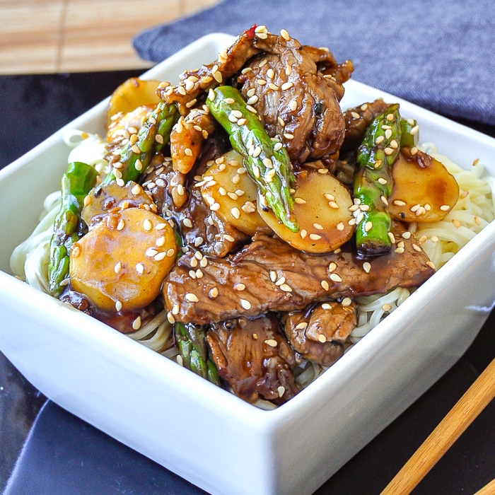 Easy Sesame Beef and Asparagus close up image served on noodles in a white bowl