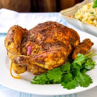 Indian Spiced Roast Chicken pictured on a white plate with fresh coriander leaves
