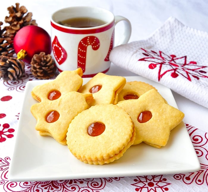 Apricot Almond Jammie Dodgers on a white plate with a cup of tea and christmas decorations in the background