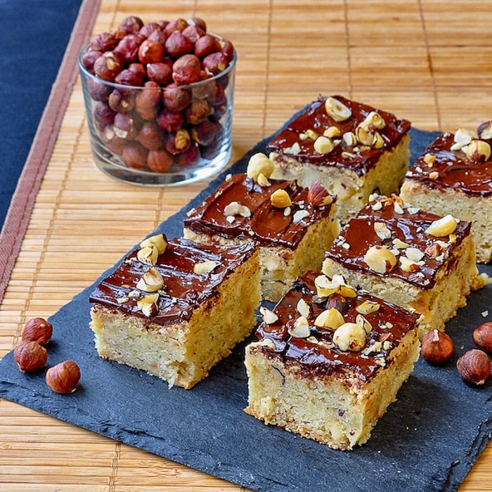 Chewy Hazelnut Bars shown on slate tray with roasted hazelnuts in background