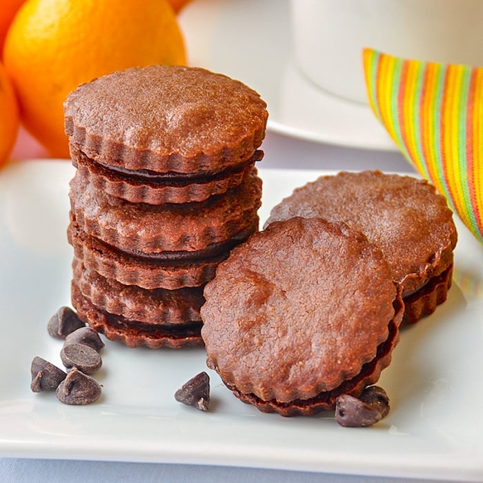Chocolate Orange Shortbread Sandwich Cookies on white serving plate with oranges in background