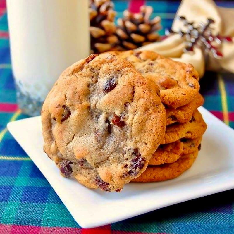 Soft Chewy Raisin Spice Cookies stacked in a white plate pictured with a glass of milk.